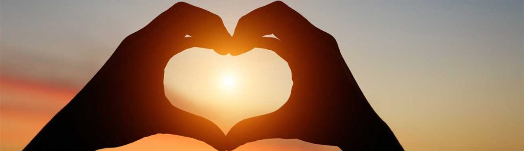 Photo of a hand heart surrounding a sunset