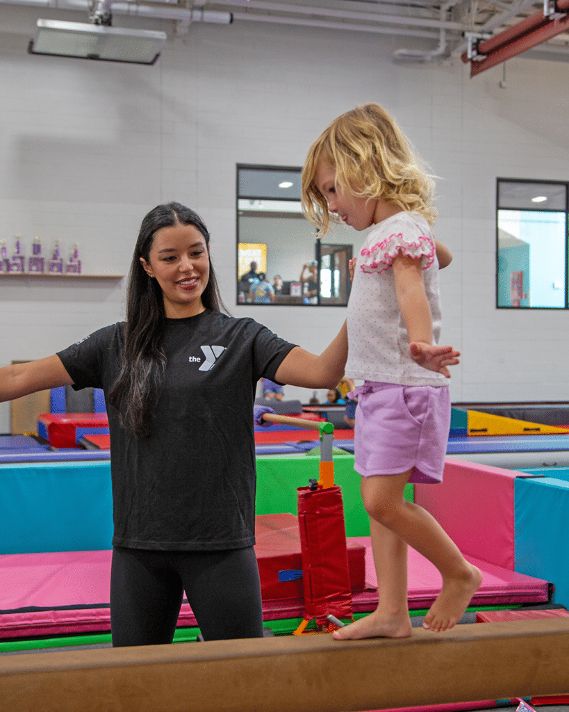 child on balance beam with instructor